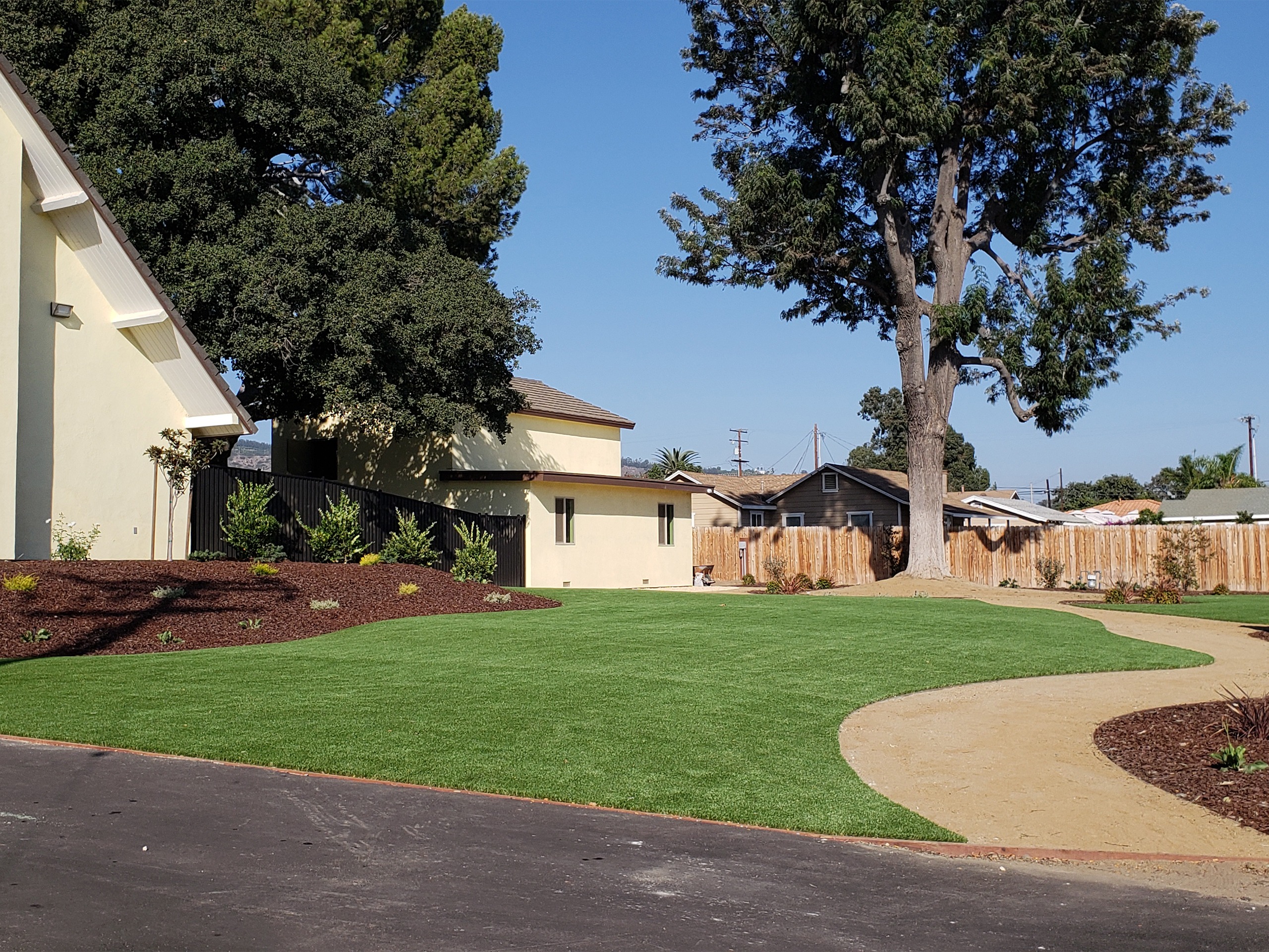 A well-maintained lawn featuring artificial grass and trees, situated in front of a charming residential house.