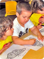 Three children engaged in coloring activities at a table, surrounded by various coloring books and art supplies.